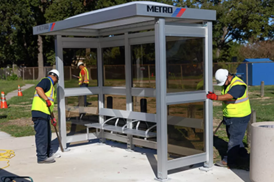 Workers in yellow safety vests installing a bus station shelter in Houston, Texas.